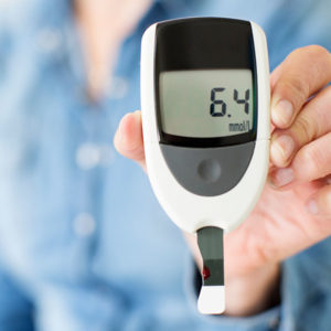 A blood glucose monitor device being held by a woman in a blue shirt